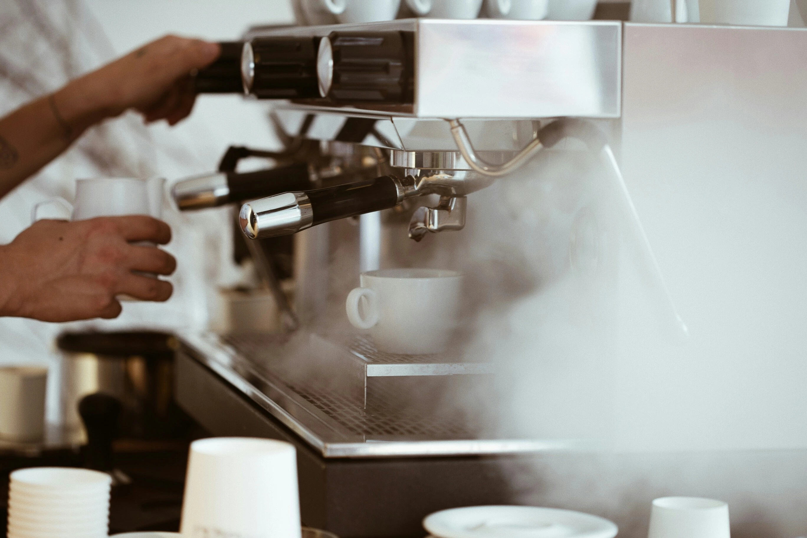 Barista using a commercial espresso machine with steam surrounding the portafilter